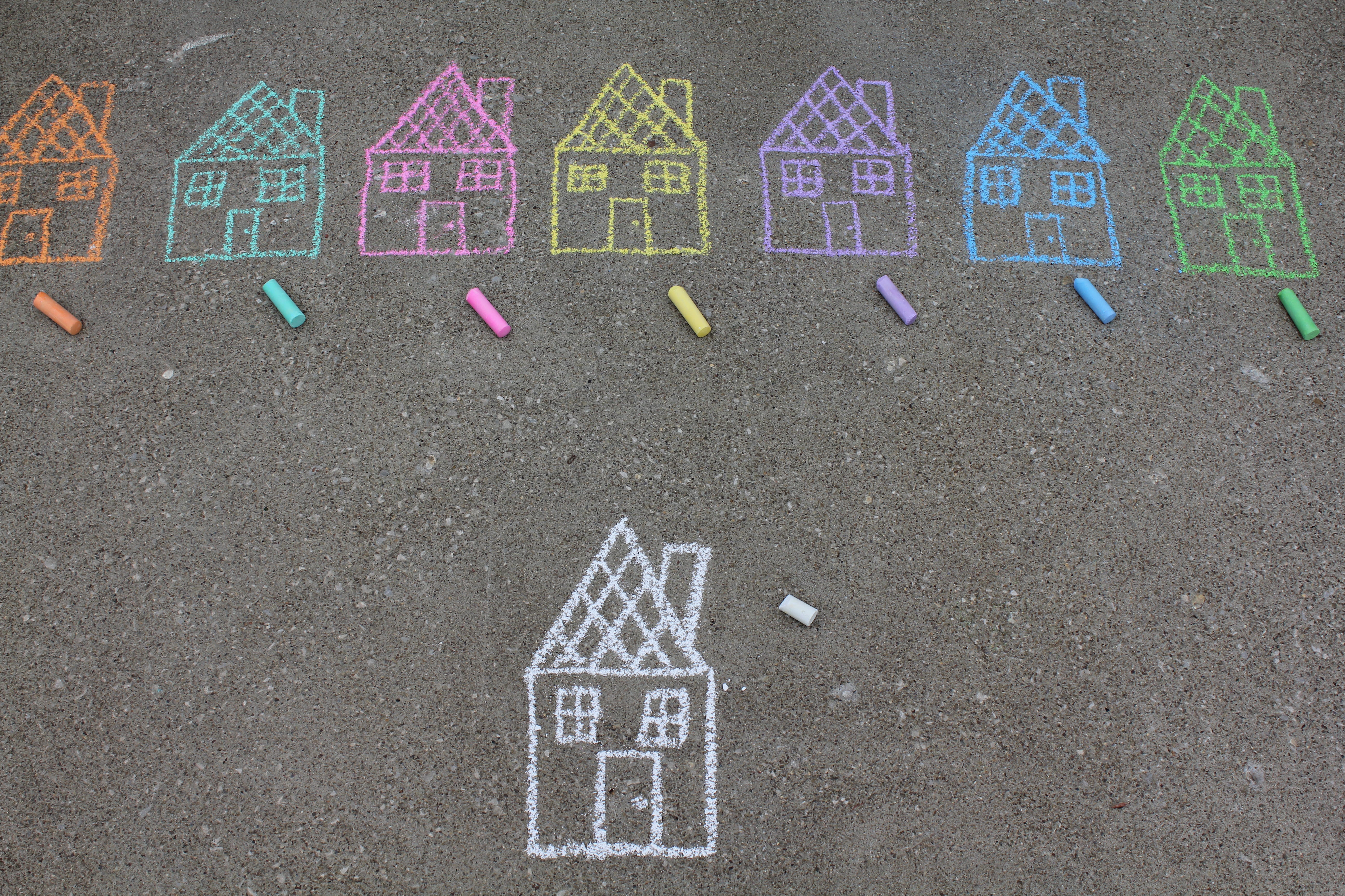 A row of colorful chalk houses, drawn on pavement. Below, there is a single house drawn in white chalk. 