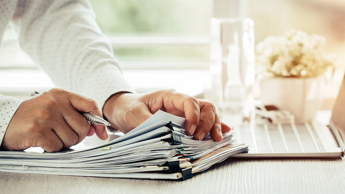 Hands with pen, stack of paper and computer